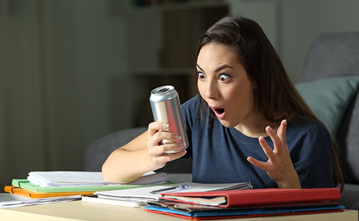 A woman with a surprised expression looks at the ingredients of a can of energy drink.